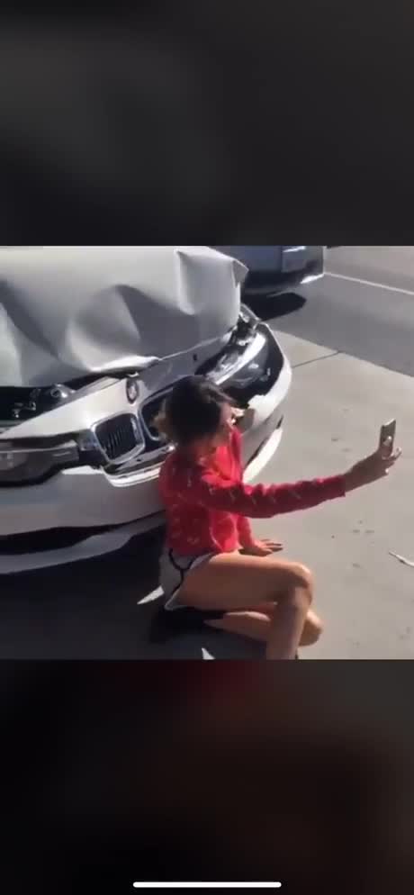 Une fille fait un selfie devant sa voiture accidentée